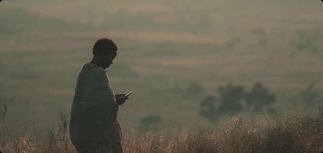 A silhouette of a person standing in a vast, hazy rural landscape at dusk, looking down at the glowing screen of a smartphone.